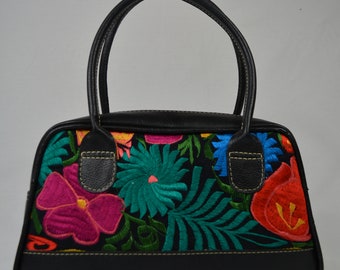 May include: Black handbag with a floral embroidered design featuring pink, red, green, blue, and yellow flowers. The bag has two black leather handles.