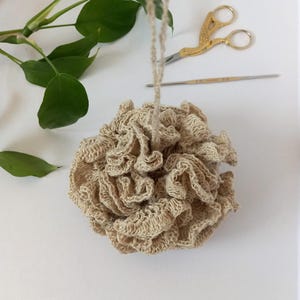 May include: A beige crocheted bath pouf with a long string hanging from the top.