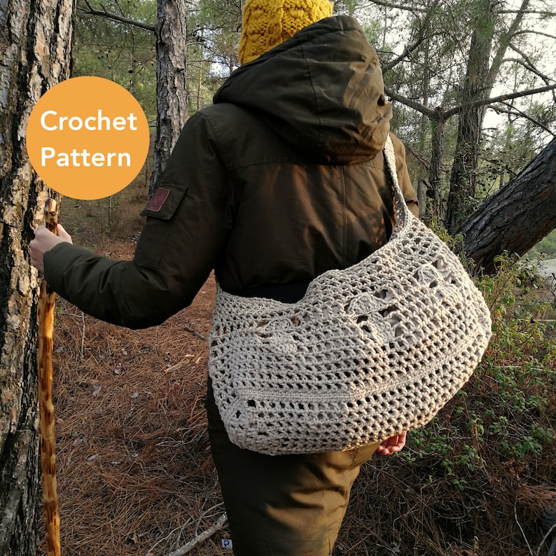 Tina is stood in the woods with the mushroom bag across her body with the bulk at her back. 3 crocheted mushrooms create a line across the middle of the bag.