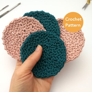 A left hand is holding four face scrubbies in it's palm with the thumb on top against a white background. The scrubbies are arranged in a circular fan shape. Two are teal and two are pastel pink.