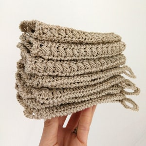 A left hand is holding up a stack of 6 folded hemp dishcloths. The bottom three have a small hanging loop on one corner