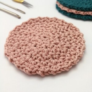 A close up photo of one of the pastel pink face scrubbies. The pattern is an even surface of mixed stitches with no clear beginning or end and an uneven edge.