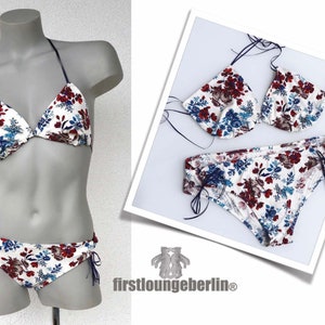 Könnte beinhalten: Ein weißer Bikini mit einem Blumenmuster in Rot-, Blau- und Weißtönen. Das Bikinioberteil ist ein Dreiecksmodell mit verstellbaren Trägern. Das Bikiniunterteil hat einen hohen Beinausschnitt und wird an den Seiten gebunden.