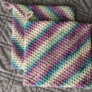May include: Two crocheted pot holders in a diamond pattern with shades of purple, green, and blue.