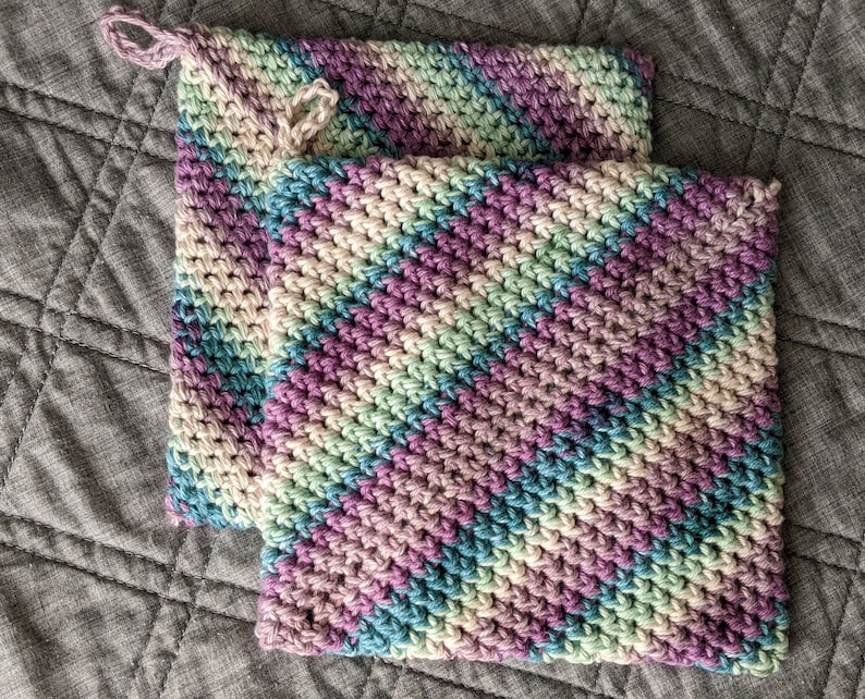 May include: Two crocheted pot holders in a diamond pattern with shades of purple, green, and blue.