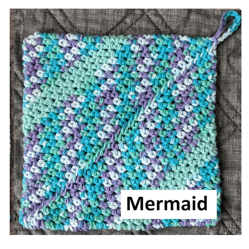 May include: A crocheted pot holder in shades of blue, green, and purple with a white loop handle. The pot holder has the word "Mermaid" printed on the bottom.