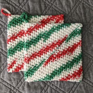 May include: Two crocheted pot holders in a red, green, and white striped pattern. The pot holders are made with a thick yarn and have a loop for hanging.