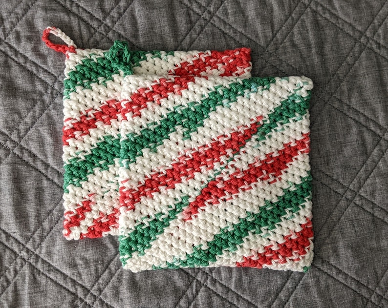 May include: Two crocheted pot holders in a red, green, and white striped pattern. The pot holders are made with a thick yarn and have a loop for hanging.