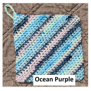 May include: A crocheted pot holder with a loop handle in shades of blue, green, and purple. The pot holder has the text "Ocean Purple" printed on it.