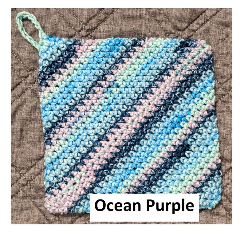 May include: A crocheted pot holder with a loop handle in shades of blue, green, and purple. The pot holder has the text "Ocean Purple" printed on it.