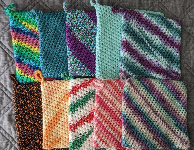 May include: Ten crocheted dishcloths in various colors and patterns, including green, purple, orange, and black. The dishcloths are arranged in two rows of five.
