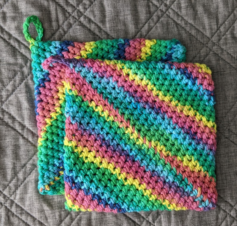 May include: Two crocheted pot holders in a rainbow color pattern. The pot holders are made with a green, blue, pink, and yellow yarn.