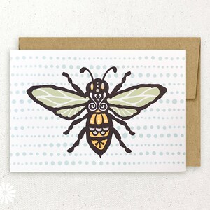 Peut inclure: Une carte de vœux avec une illustration stylisée d'abeille en noir, jaune et vert sur un fond blanc avec un motif de points bleus. L'abeille a des détails complexes et un design fantaisiste.
