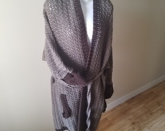 May include: A long, brown and gray crocheted robe with a tie belt and pockets. The robe has a brown trim around the edges and the pockets.