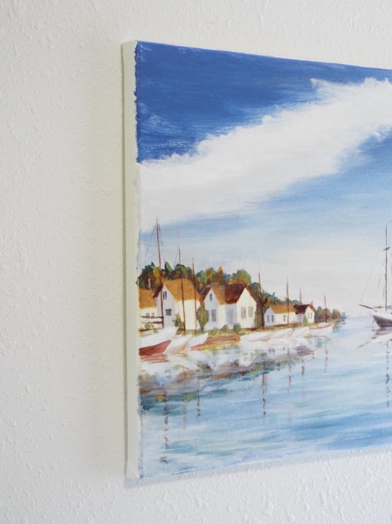 May include: A painting depicting a seascape with white houses and boats moored along the shore. The sky is blue with white clouds and the water is a light blue.