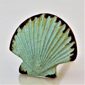 May include: A decorative seashell-shaped object with a distressed finish. The shell features a light turquoise color with dark brown edges and detailed ridged texture, creating a vintage aesthetic. The object is likely a decorative element or a piece of coastal-themed decor.