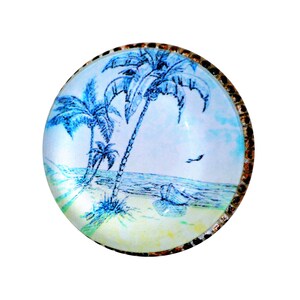 May include: Round glass cabochon with a beach scene featuring palm trees, a boat, and a flying bird. The artwork is in shades of blue and white, with a decorative, textured border.
