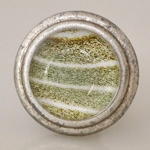 May include: A round, silver-toned cabinet knob with a glass insert. The insert features a pattern of horizontal stripes in shades of green, brown, and white. The knob has a slightly distressed, vintage appearance.