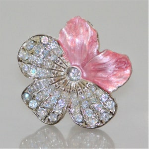 May include: A flower-shaped brooch with a silver-tone metal frame. One petal is painted pink, while the other two are encrusted with clear, sparkling rhinestones. A large rhinestone is in the center of the flower.