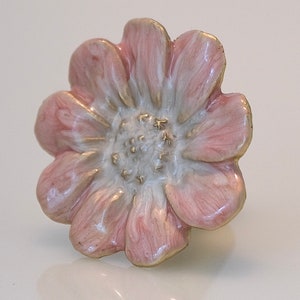 May include: A close-up of a flower-shaped decorative knob. The knob features a pink and white color scheme with gold accents. The petals are pink, and the center is white with gold detailing.