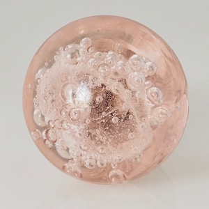 May include: A spherical glass paperweight in a soft blush pink hue. The interior of the clear glass sphere contains a cluster of trapped air bubbles of varying sizes, creating a textured, effervescent appearance throughout the center of the object.