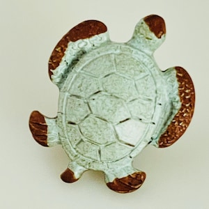 May include: A ceramic turtle figurine with a light blue body and a brown shell and flippers. The turtle's shell has a textured, geometric pattern. The edges of the shell and flippers are also brown.
