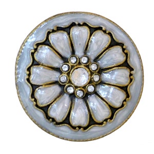 May include: A round, decorative button with a floral design. The button features a light blue enamel background with a gold-colored trim. The flower petals are white with gold outlines, and the center is adorned with clear crystals.