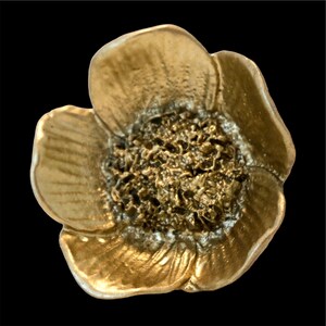 May include: A detailed, close-up view of a golden-colored flower with textured petals and a textured center. The flower is set against a black background, highlighting its intricate details and metallic sheen. The flower's design is reminiscent of a poppy.