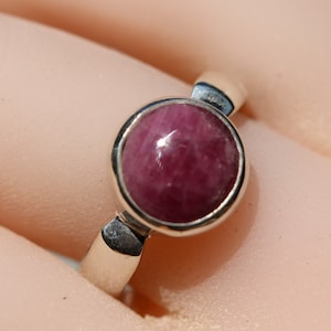 May include: A silver ring featuring a round, cabochon-cut pink gemstone set in a bezel setting.