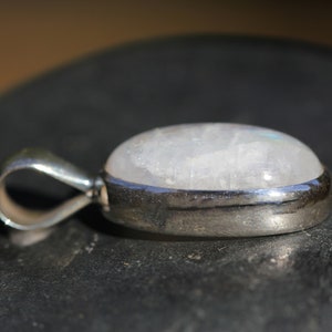 May include: A silver pendant with a white moonstone cabochon. The pendant has a simple bail for attaching to a chain.