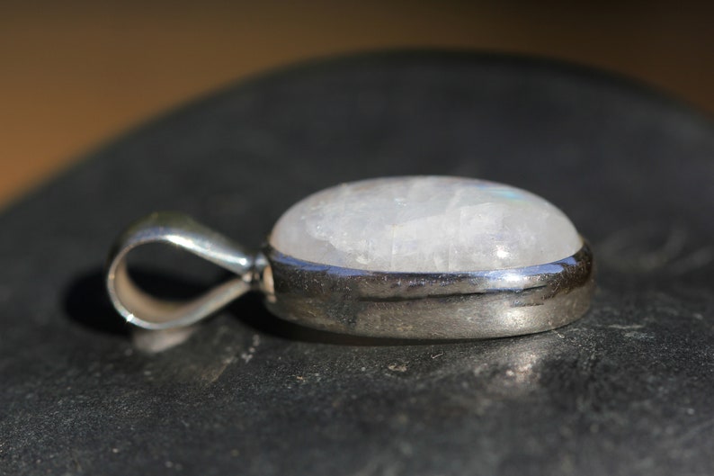 May include: A silver pendant with a white moonstone cabochon. The pendant has a simple bail for attaching to a chain.
