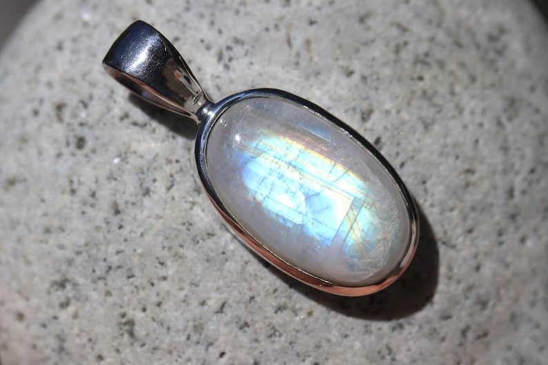 May include: A silver pendant with a large oval moonstone. The moonstone is iridescent with blue and gold hues.