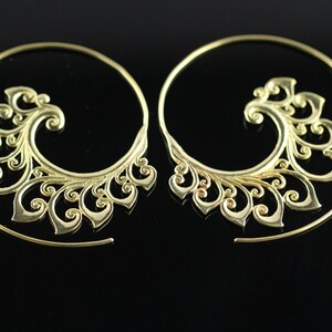 May include: A pair of gold-toned hoop earrings with a decorative, swirling, floral design. The earrings are made of metal and have a circular shape.