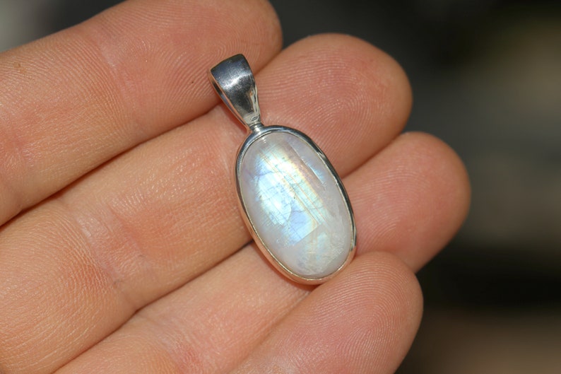May include: A silver pendant with a white oval moonstone. The moonstone has a rainbow sheen.
