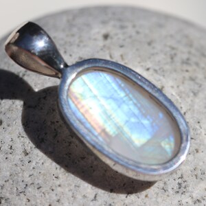 May include: A silver pendant with a large oval-shaped iridescent gemstone. The gemstone has a white base with blue, green, and pink iridescent flashes.