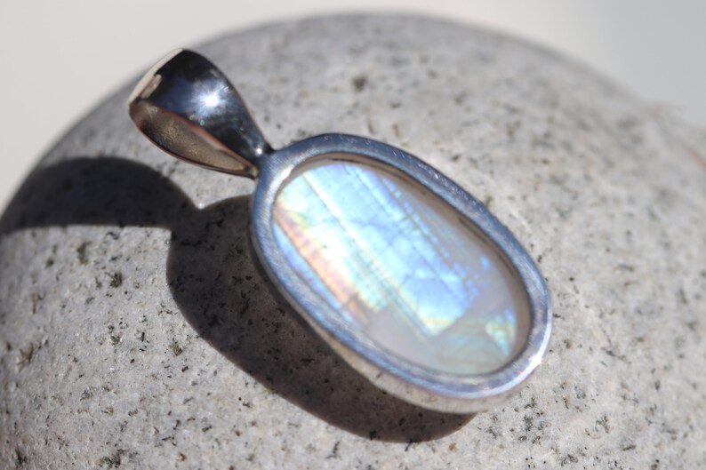 May include: A silver pendant with a large oval-shaped iridescent gemstone. The gemstone has a white base with blue, green, and pink iridescent flashes.