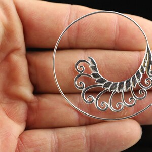 Op de afbeelding: Zilveren oorring met een decoratief, sierlijk ontwerp met een reeks swirls en bladeren.