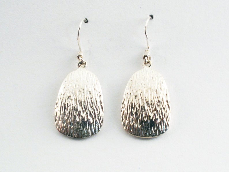May include: A pair of silver dangle earrings with a textured, oval-shaped design.