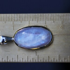 May include: A silver pendant with a large oval moonstone gemstone. The stone is a pale blue color with iridescent flashes of color. The pendant is about 1 inch long and is shown next to a ruler.