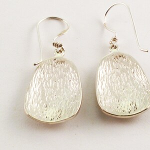 May include: A pair of silver dangle earrings with a textured oval shape. The earrings have a simple hook closure.