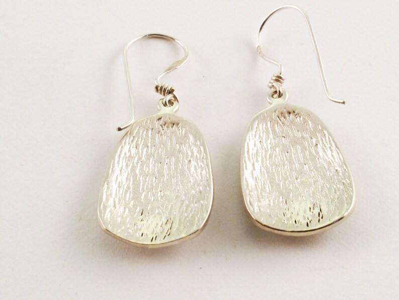 May include: A pair of silver dangle earrings with a textured oval shape. The earrings have a simple hook closure.