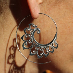 May include: Silver hoop earrings with a decorative, filigree design. The design is a swirl of leaves and flowers.