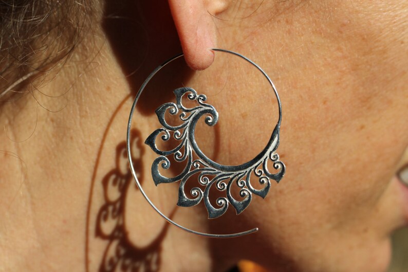 May include: Silver hoop earrings with a decorative, filigree design. The design is a swirl of leaves and flowers.