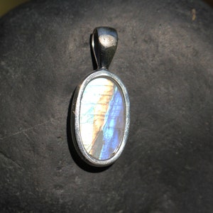 May include: A silver oval pendant with a blue and white butterfly wing inside. The pendant is on a gray stone background.