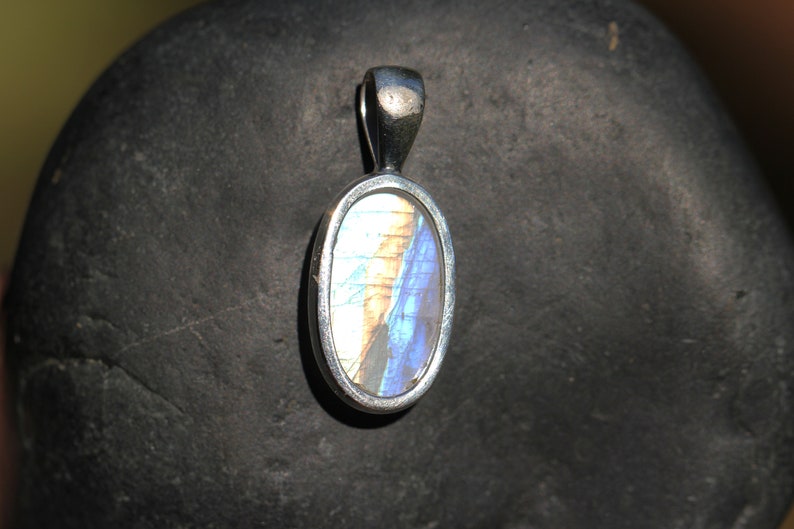 May include: A silver oval pendant with a blue and white butterfly wing inside. The pendant is on a gray stone background.
