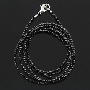 May include: A black beaded necklace with a silver clasp. The necklace is composed of small, round, black beads strung together. The beads are closely packed, forming a smooth, continuous line. The clasp is a simple, secure design.