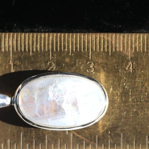 May include: A silver pendant with a white oval moonstone. The pendant is approximately 1 inch long and is shown next to a ruler.