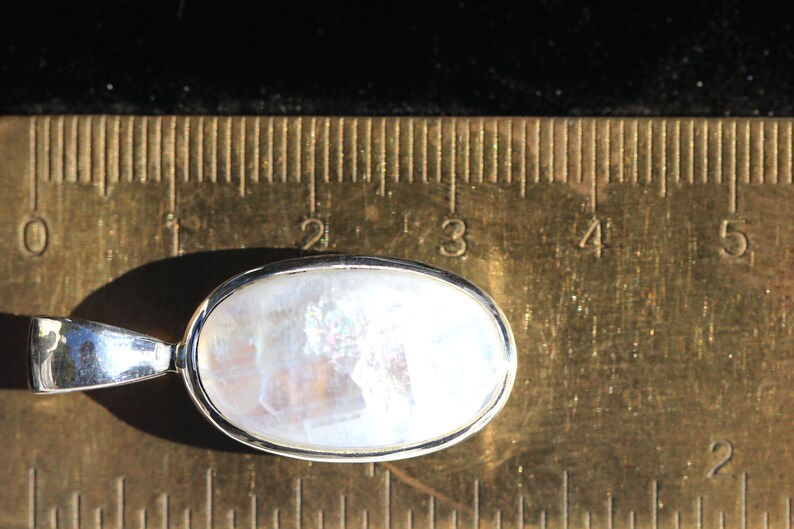 May include: A silver pendant with a white oval moonstone. The pendant is approximately 1 inch long and is shown next to a ruler.