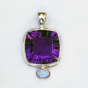 May include: A silver pendant featuring a large, square-cut, faceted amethyst gemstone with a deep purple hue. Below the amethyst is a small, oval opal. The pendant has a silver bail for a chain.
