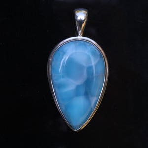 May include: A silver pendant with a light blue, teardrop-shaped gemstone. The gemstone has a swirling, marbled pattern.